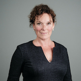 Eine Frau mit schwarzem Oberteil vor einem grauen Hintergrund.