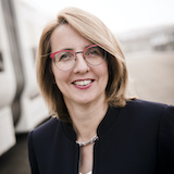 Eine Frau mit roter Brille, schwarzem Blazer und schulterlangen blonden Haaren.