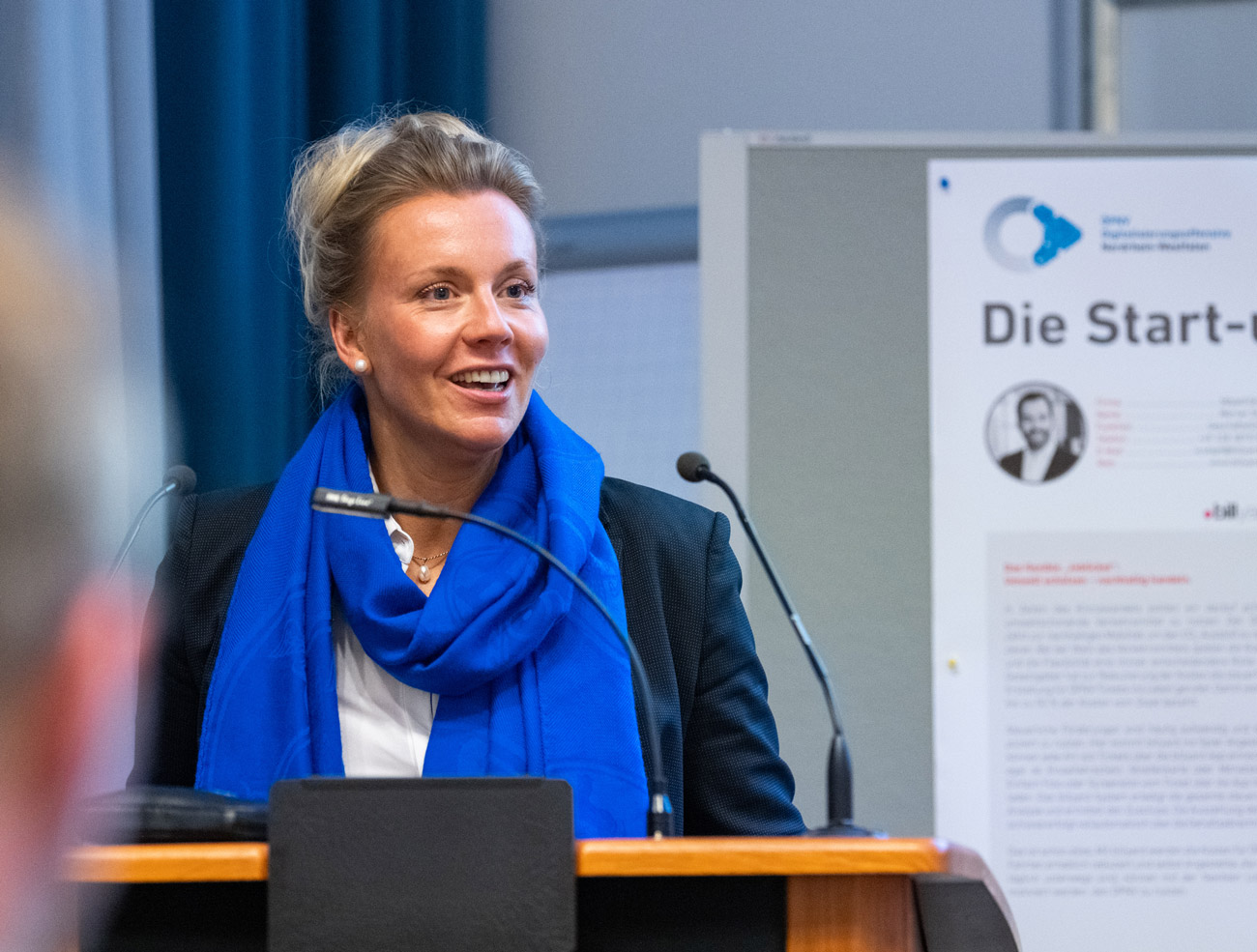 NRW-Verkehrsministerin Ina Brandes hält an einem Holzpodium eine Rede.